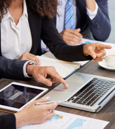 Faceless shot of coworking businesspeople surfing laptop while discussing project at table in office